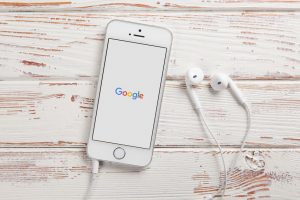 Tischplatte mit Smartphone, Google auf dem Bildschirm und Linear-Kopfhörer daneben