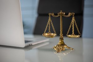 Schreibtisch mit aufgeklapptem Laptop, daneben goldene Waage