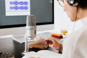 Frau vor Monitor mit offenem Audioeditor, trägt Kopfhörer und spricht in Mikrofon